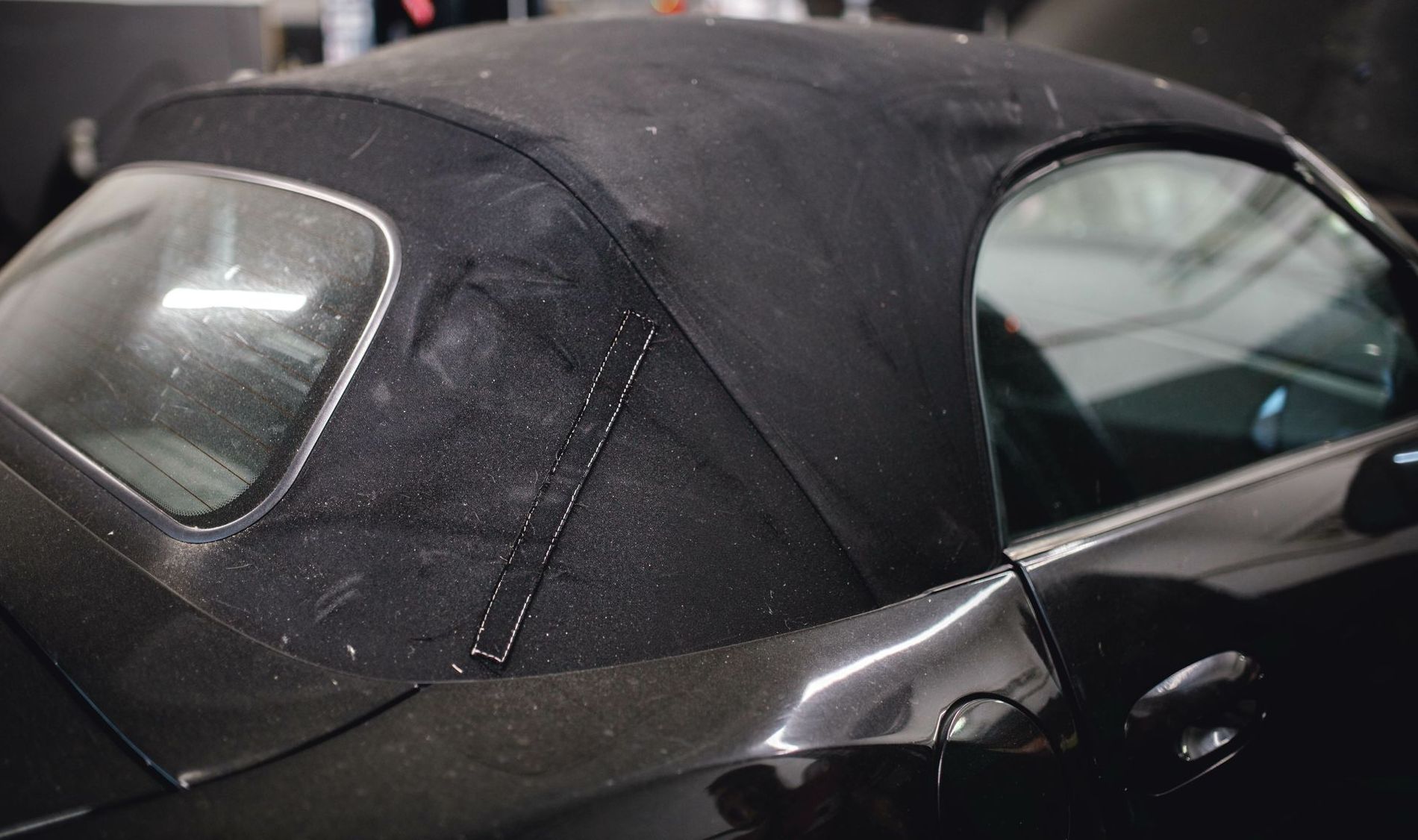 A black convertible car with a black top is parked in a garage.