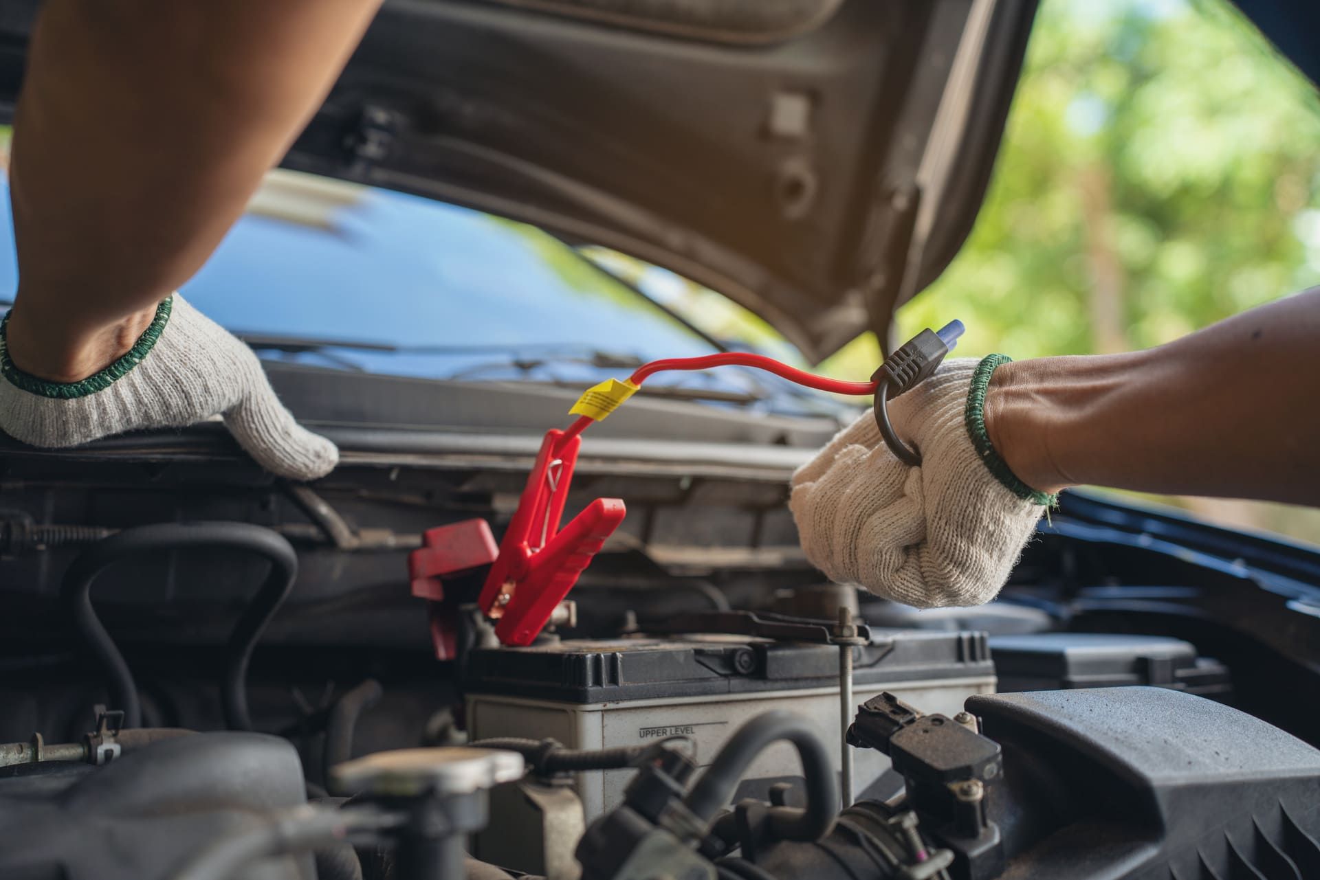 Close-up of mechanic holding voltmeter to check voltage car battery energy problem for service maintenance. Car mechanic noting repair parts during open car hood engine repair unrecognisable
