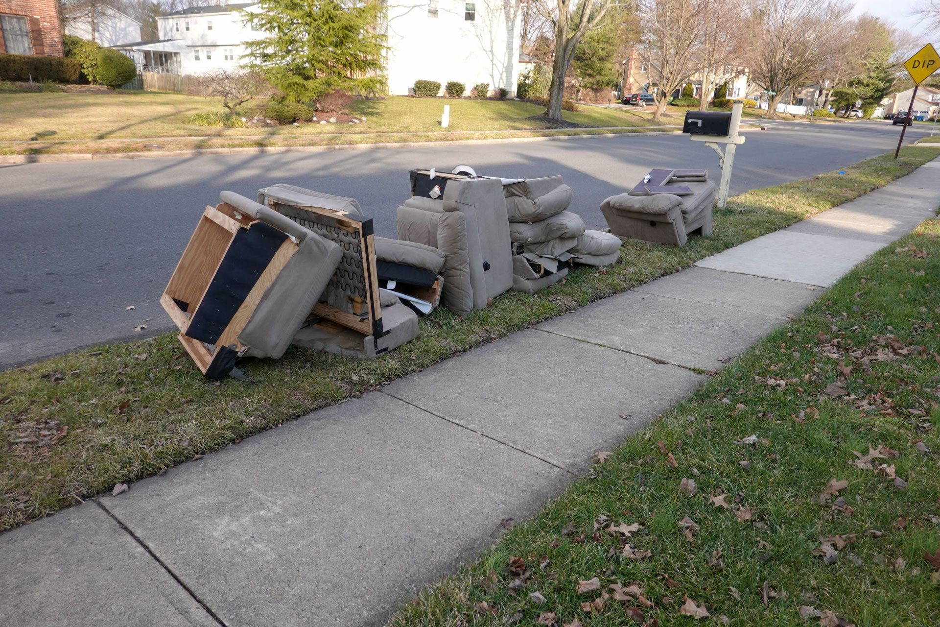 Pile of discarded furniture and trash on a suburban sidewalk near a residential street