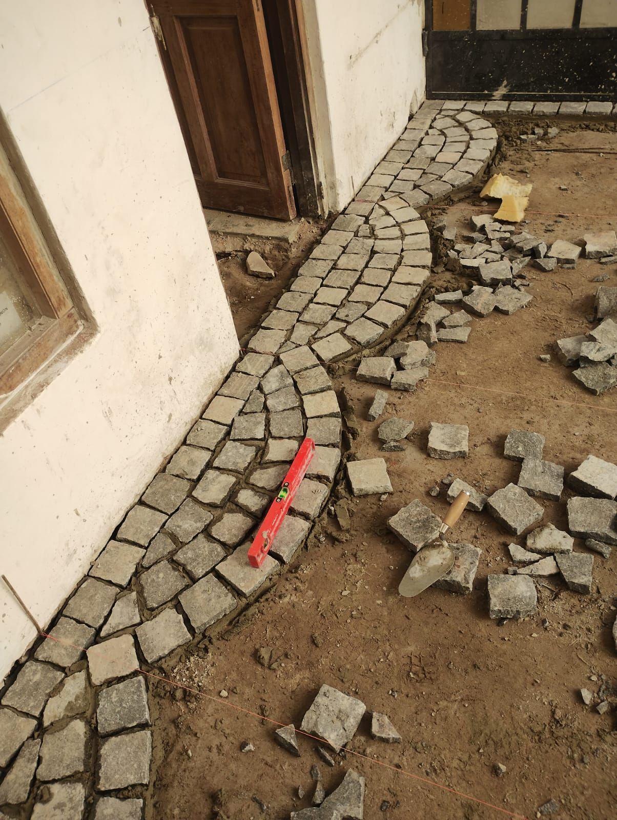 Se está construyendo un camino empedrado junto a un edificio. Hay un nivel en el camino; hay piedras sueltas cerca.
