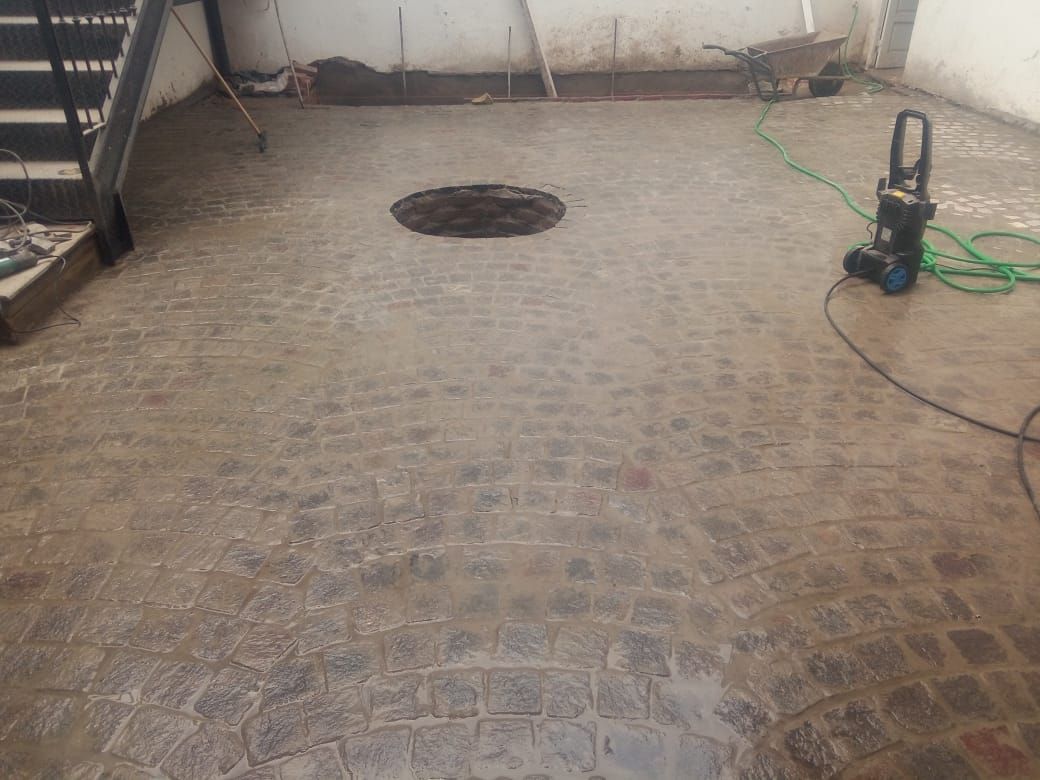 Patio de ladrillos mojados con un agujero oscuro en el centro, manguera de agua, hidrolavadora.