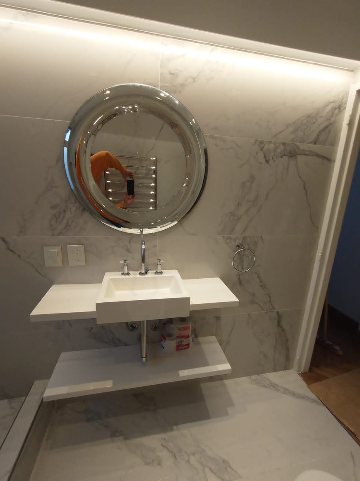 Baño con espejo redondo, lavabo flotante y paredes con estampado de mármol.