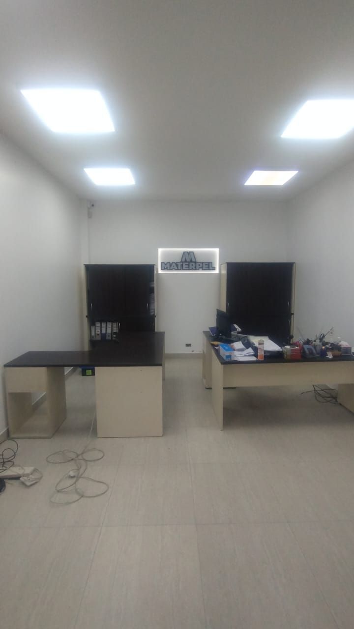 Oficina blanca y vacía con dos escritorios oscuros y grandes pantallas negras. Luces fluorescentes en el techo.