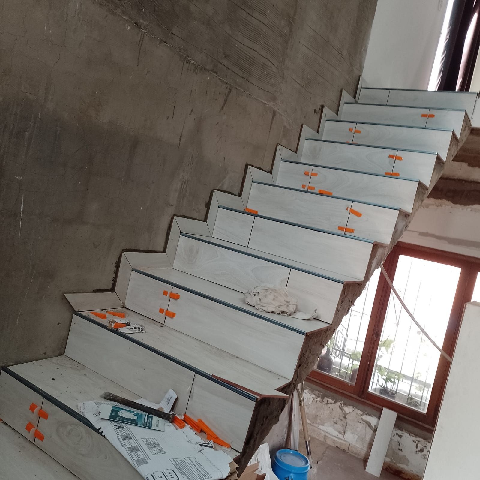 Escalera en construcción con escalones de baldosas blancas, espaciadores de baldosas de color naranja.