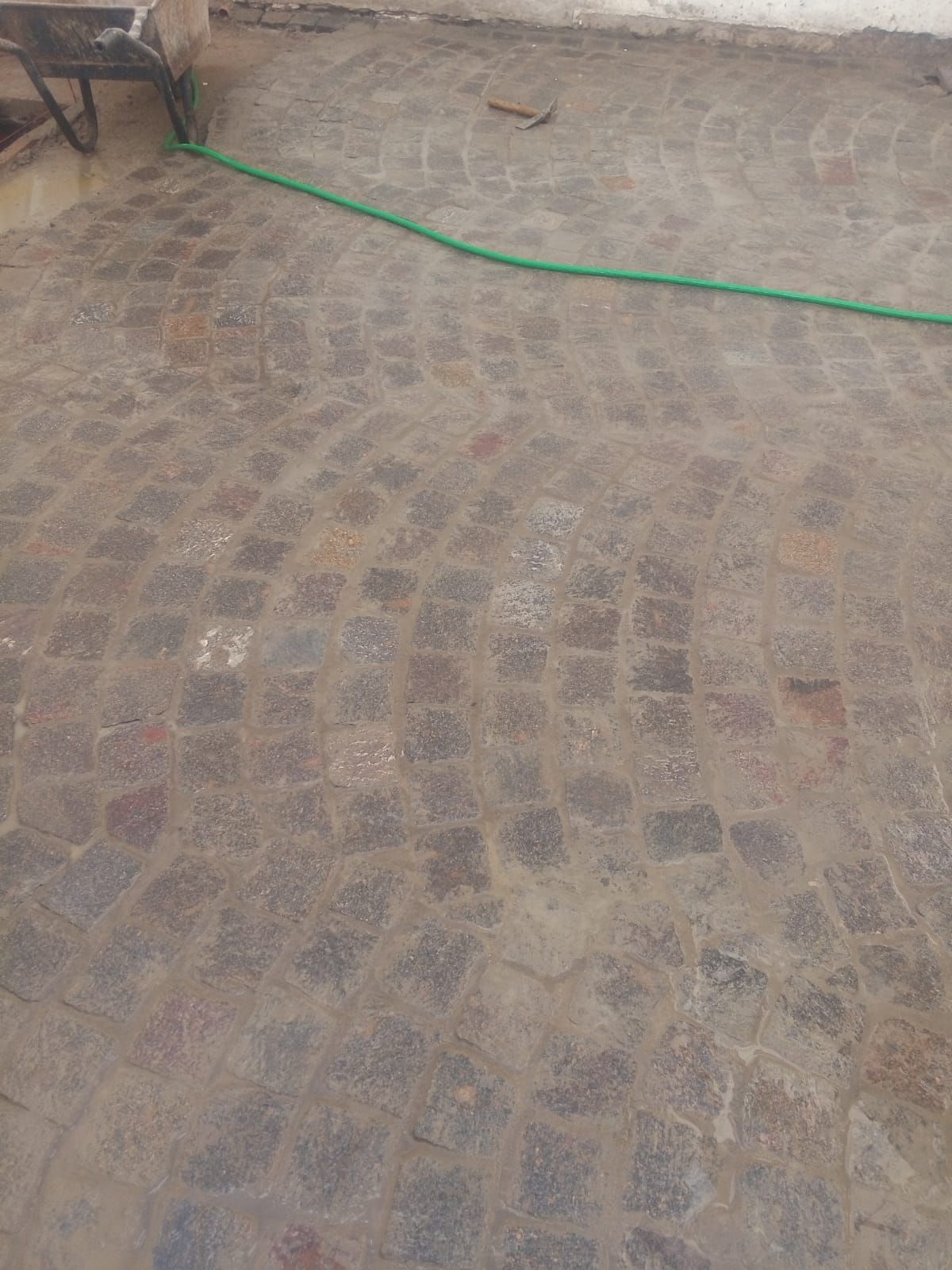Pavimento adoquinado, con manguera verde, visto desde arriba.
