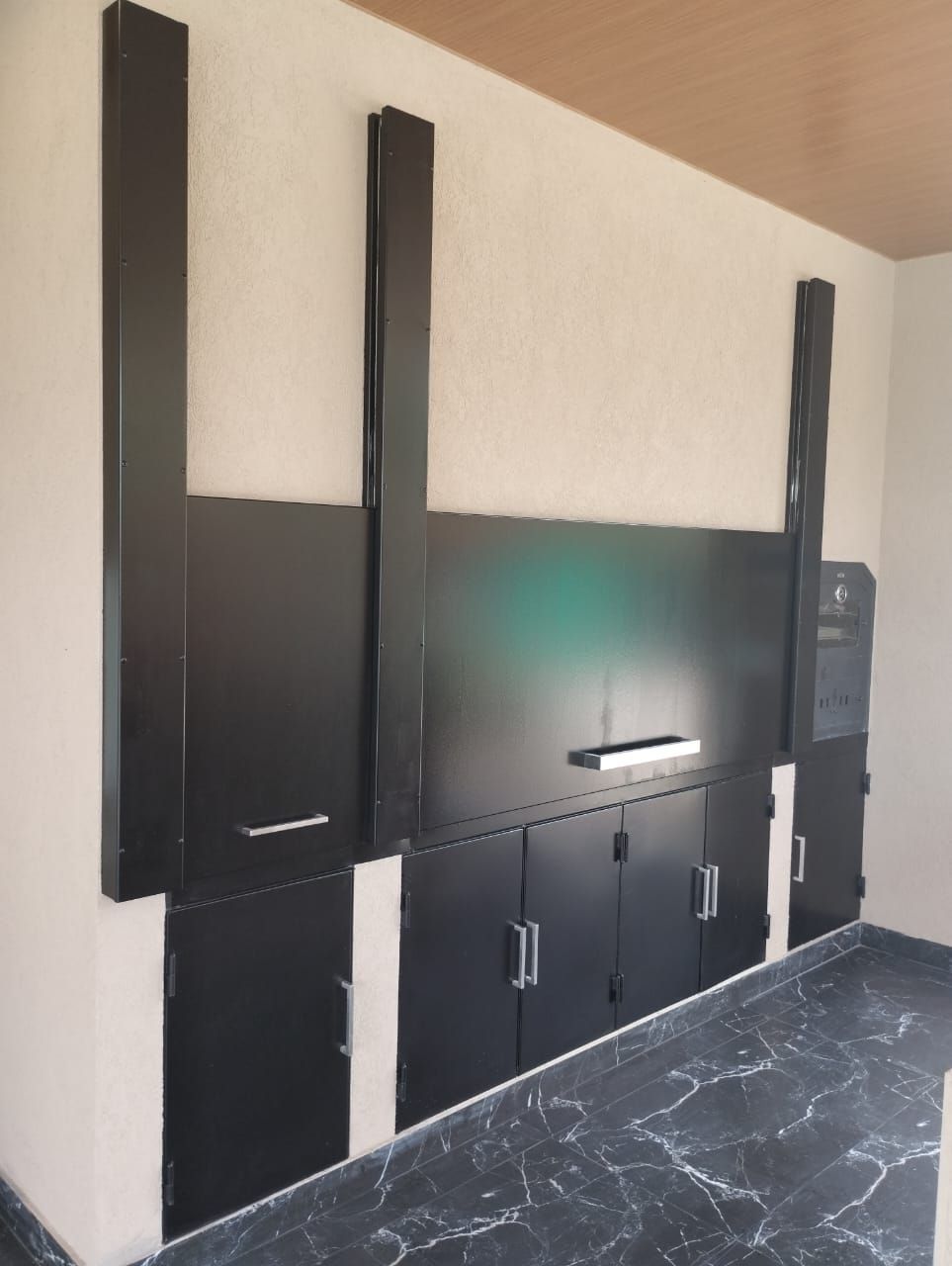 Almacenamiento de pared negro con múltiples puertas y compartimentos contra una pared de color claro y un piso oscuro.