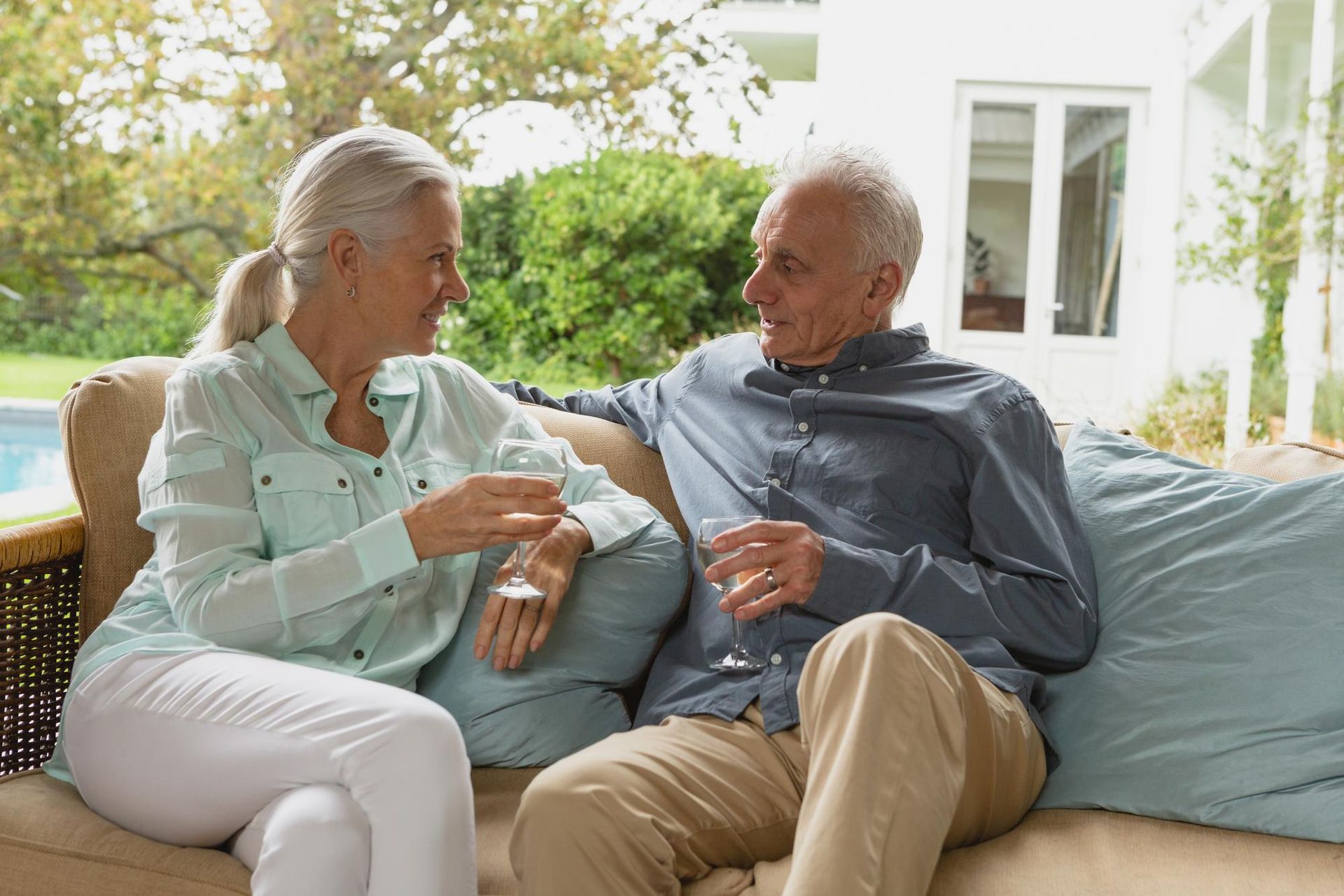 Senior couple sitting on a couch outdoors, smiling, holding drinks.