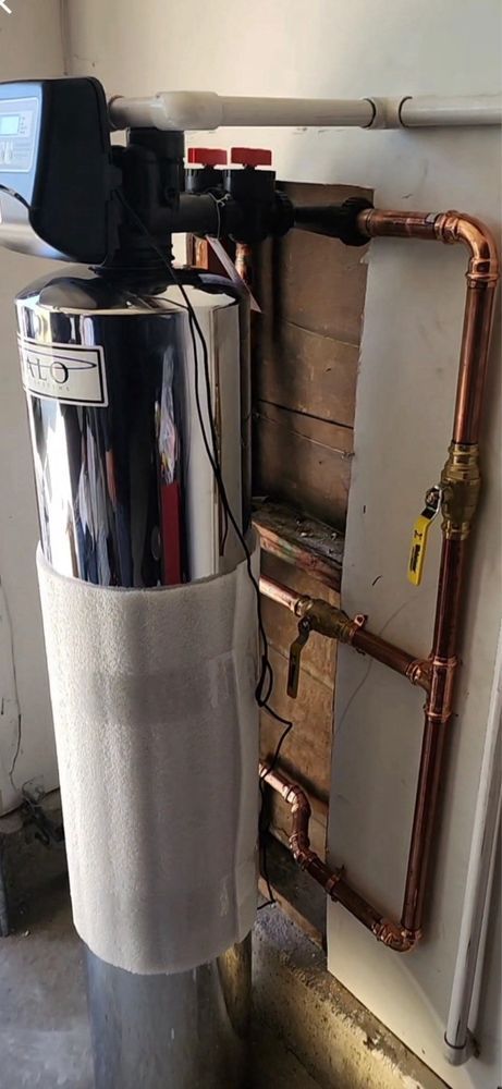 Water softener system with copper pipes in a utility room.