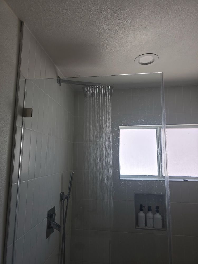 Shower with glass enclosure, water pouring down, white tile, a window, and built-in shelf with bottles.