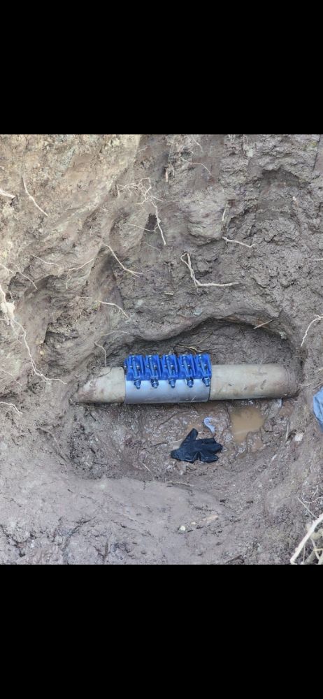 A pipe repaired with a blue clamp, buried in soil.