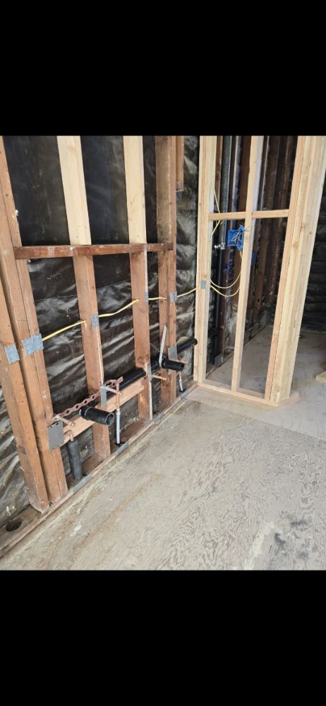 Construction site showing wooden framing, plumbing, and electrical work in a wall.