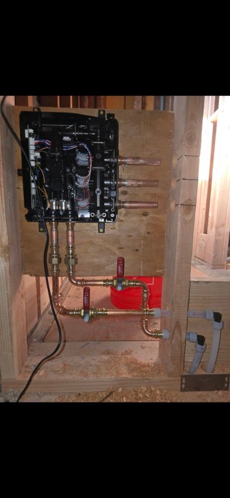 Black plumbing components with copper pipes, red tank, and wooden frame.