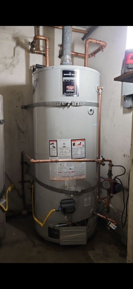 A gas water heater in a basement with copper piping and yellow electrical wires.