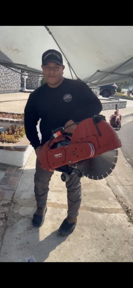 Man in black shirt holding a large red concrete saw outdoors.