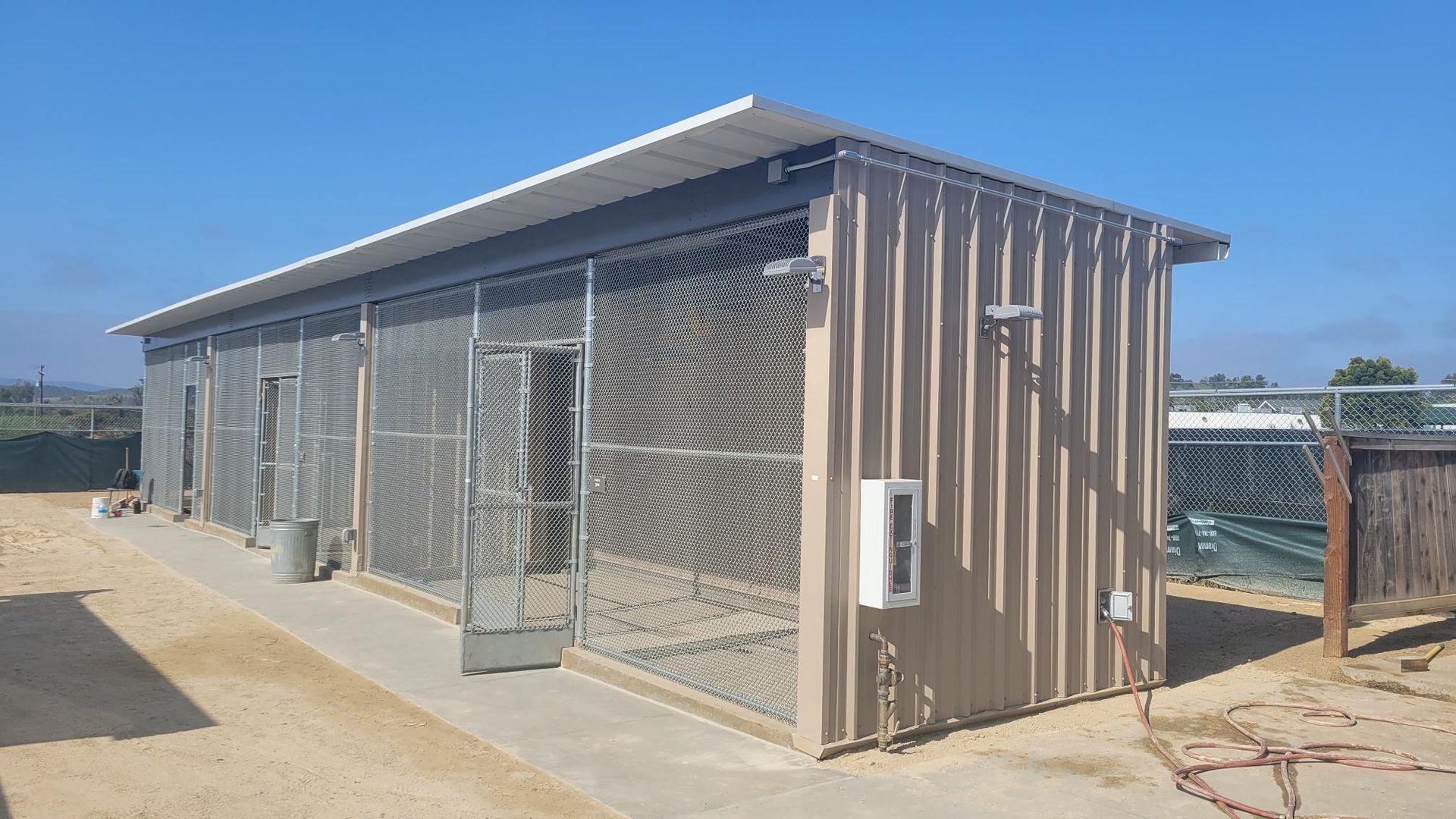 A large metal building with chain link fences and a blue sky in the background.