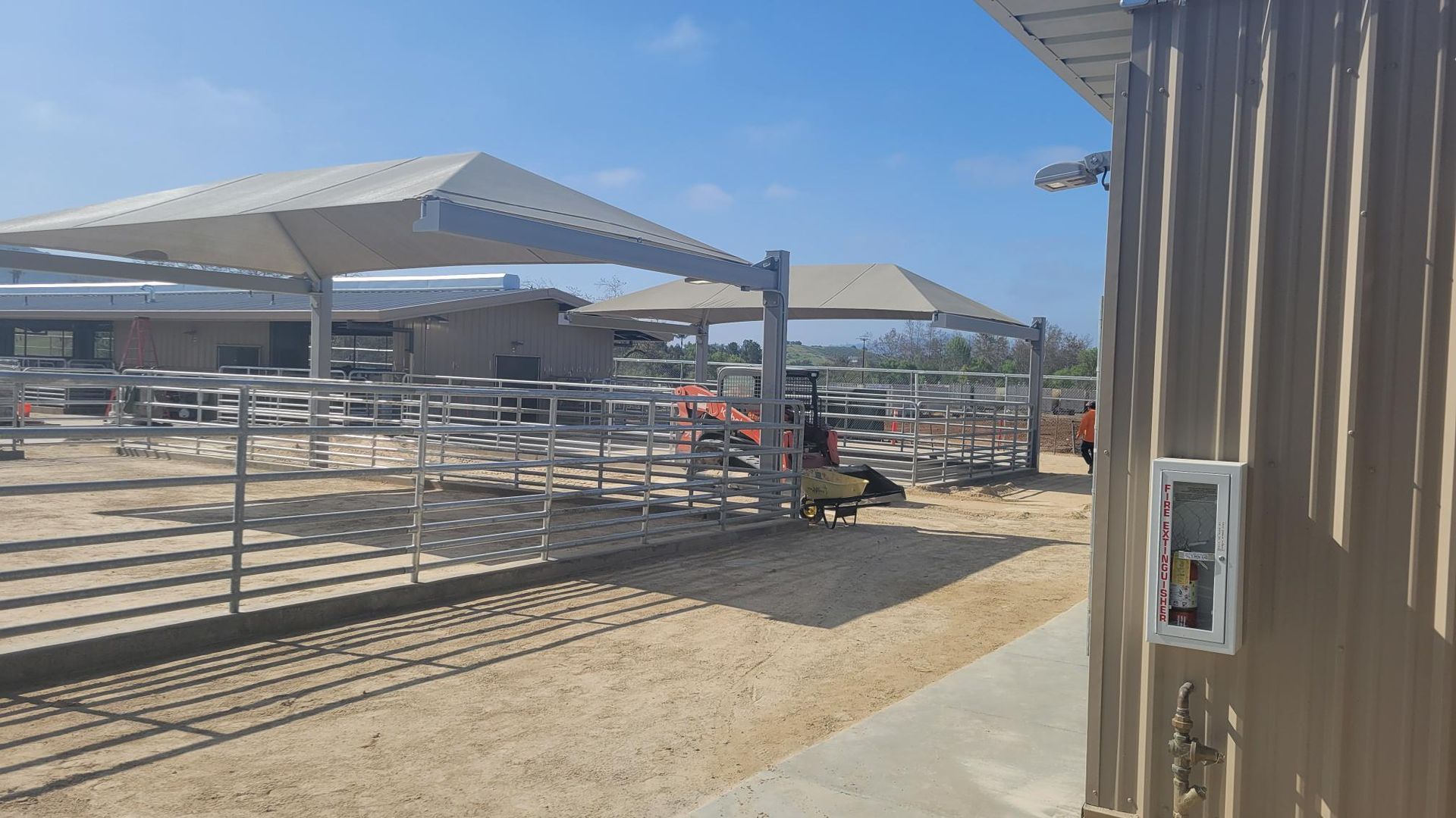 A fenced in area with a covered area and a building in the background.