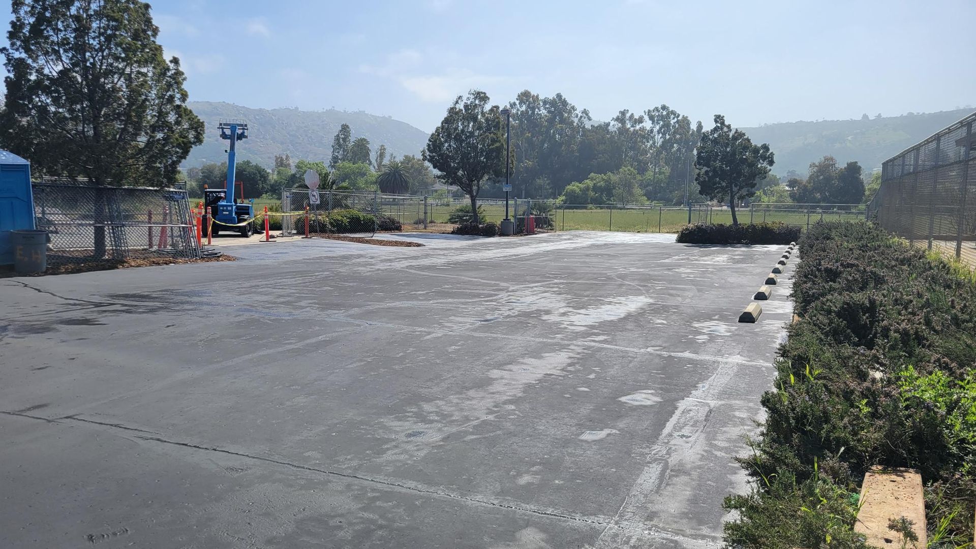 A large empty parking lot with trees and mountains in the background.