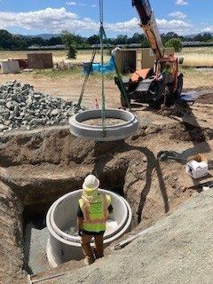 A crane is lifting a concrete ring into a hole in the ground.
