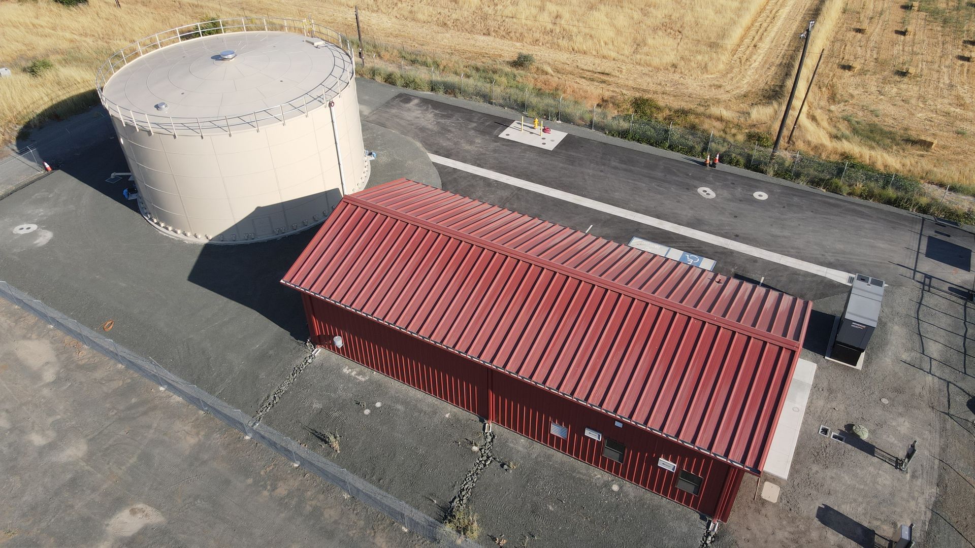 An aerial view of a building with a red roof and a large tank in the background.