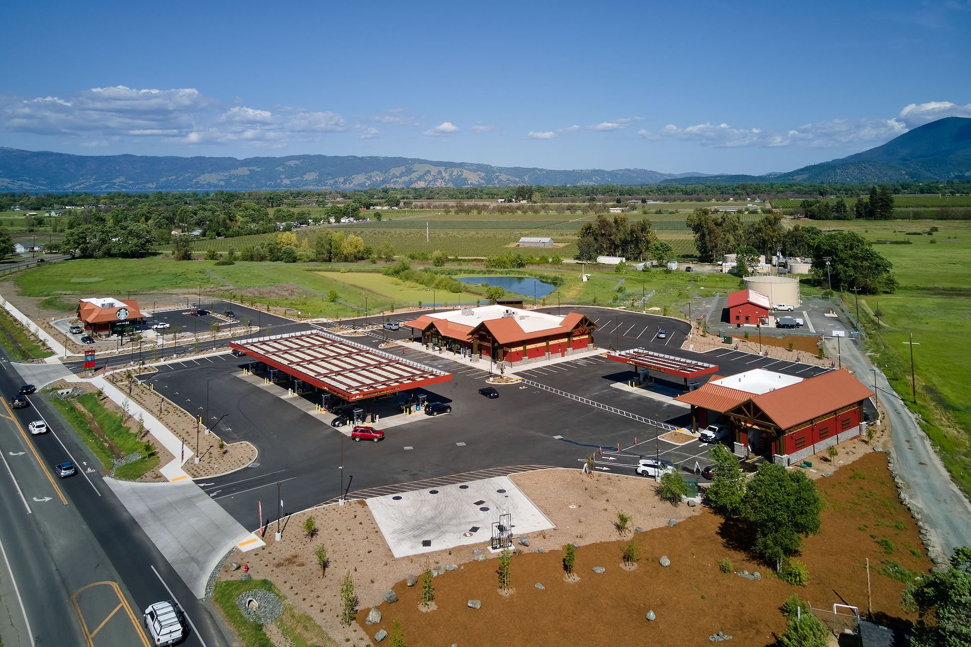 Aerial view of a red-roofed building complex with parking lot, surrounded by green fields and mountains.
