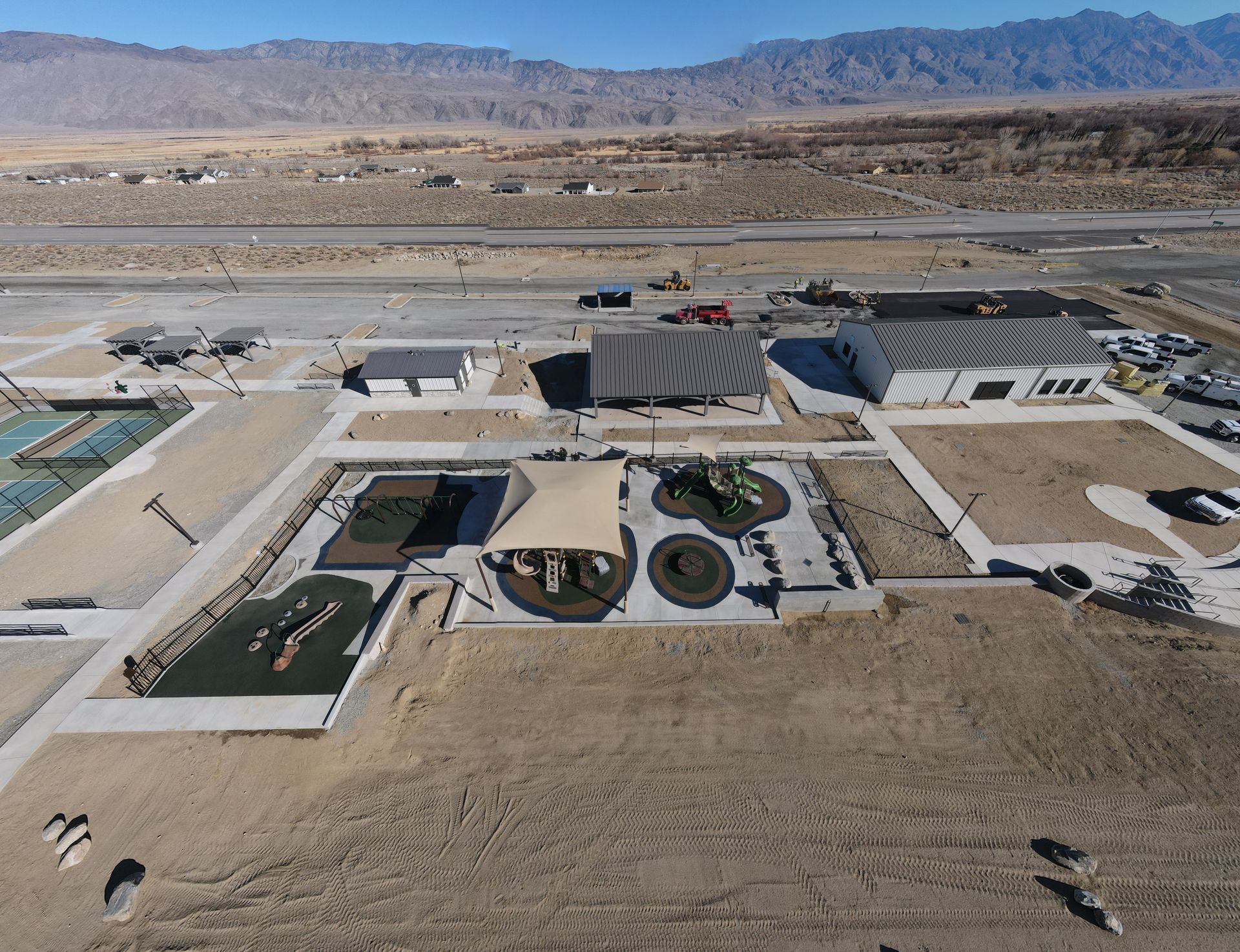 Aerial view of a desert park with playgrounds, buildings, and a runway in the background.