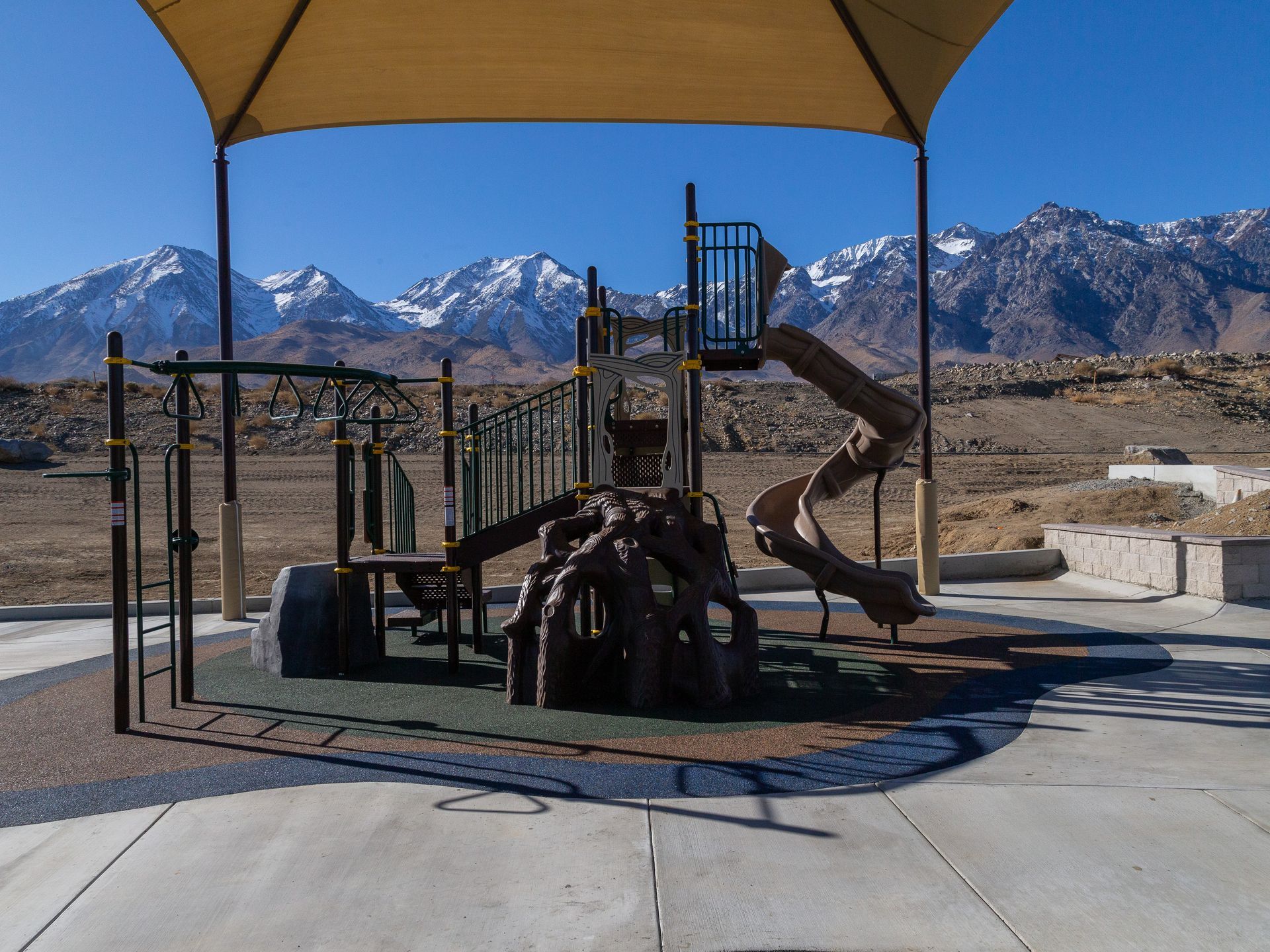Playground with tan shade, in front of snowy mountains.