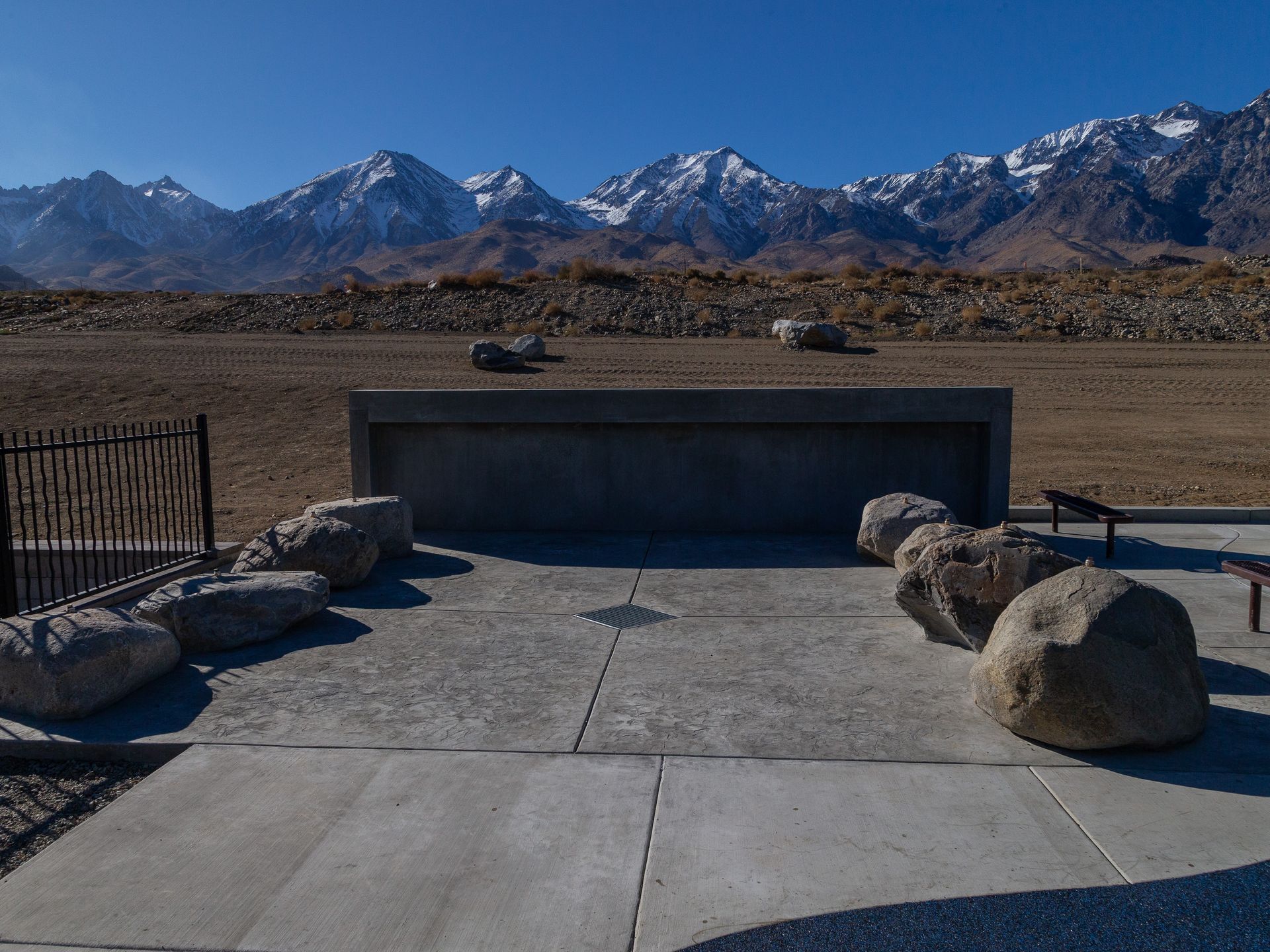 Concrete bench and large rocks with mountain backdrop under blue sky.