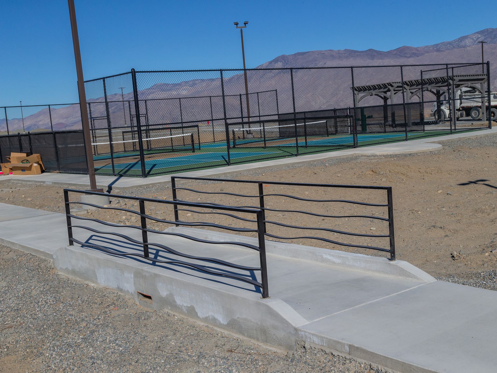 A concrete walkway with handrails leading to a sports court, set against a desert mountain backdrop.
