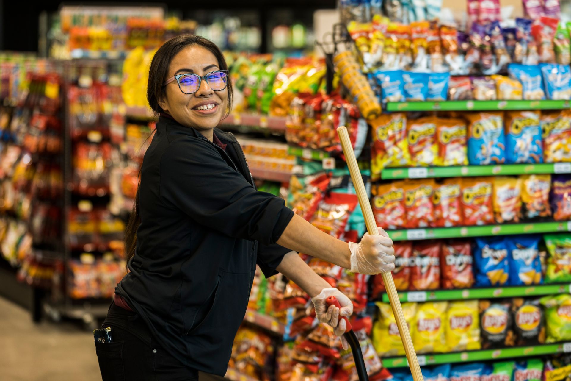 A woman is cleaning shelves in a grocery store with a mop.