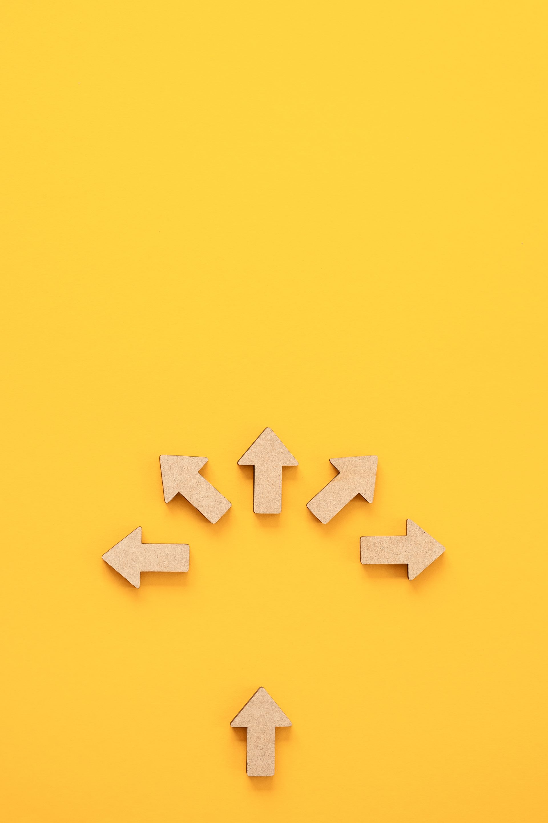 Cardboard arrows pointing in different directions on a yellow background, with one arrow below them pointing upwards.
