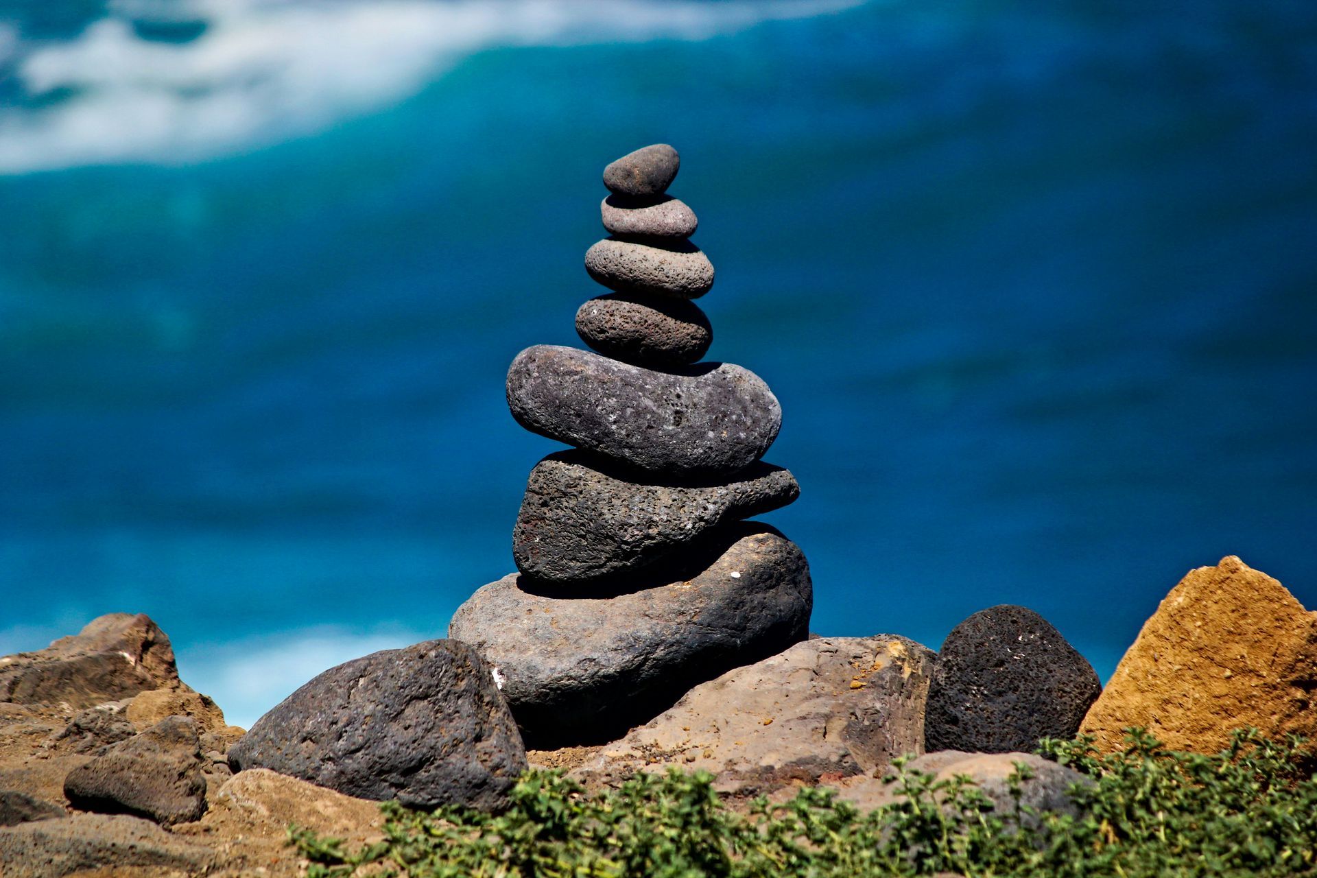 Stack of balanced gray stones against a blue ocean backdrop.