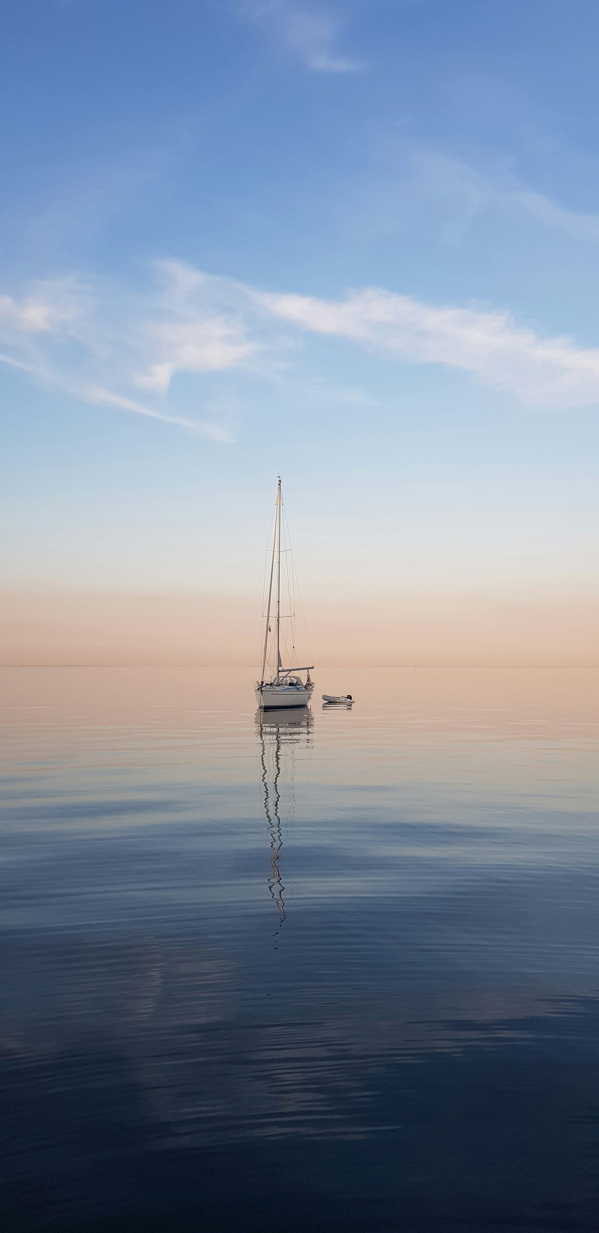 Sailboat on calm water reflecting a colorful sky.