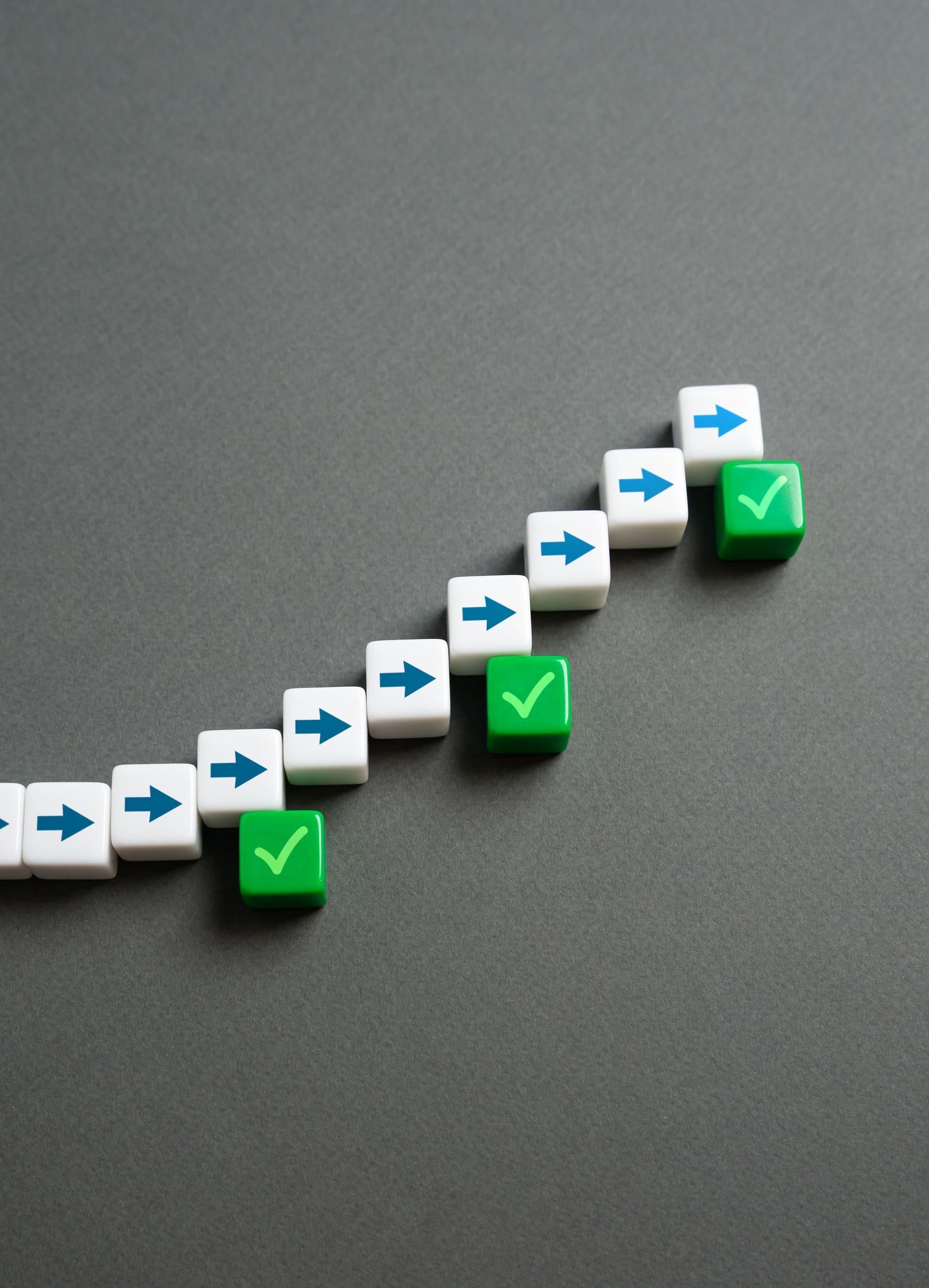 Blocks forming an upward-sloping line, with blue arrows and green checkmarks, representing progress on gray background.