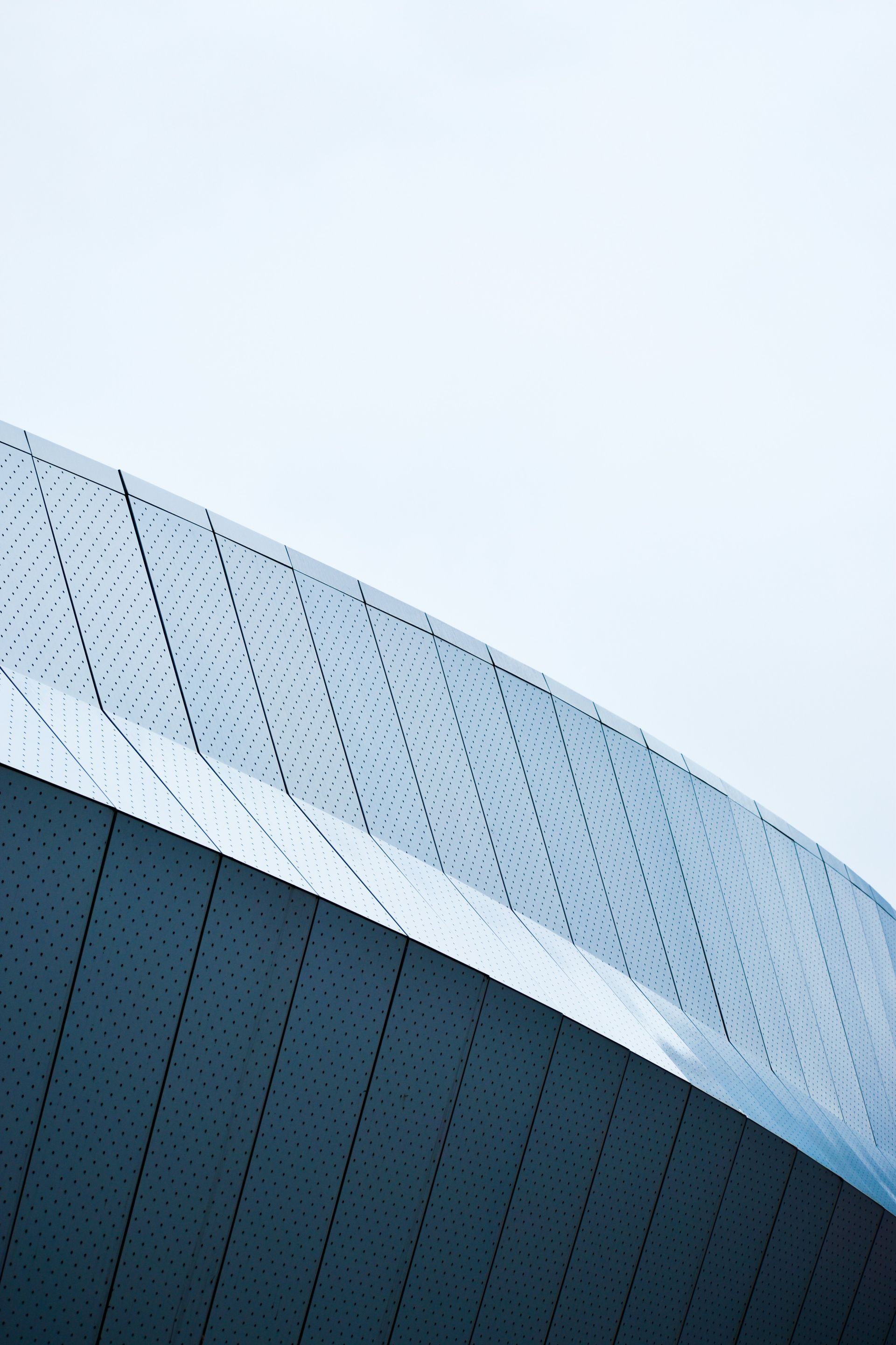 Curved, modern building exterior with a reflective, patterned facade against a pale sky.