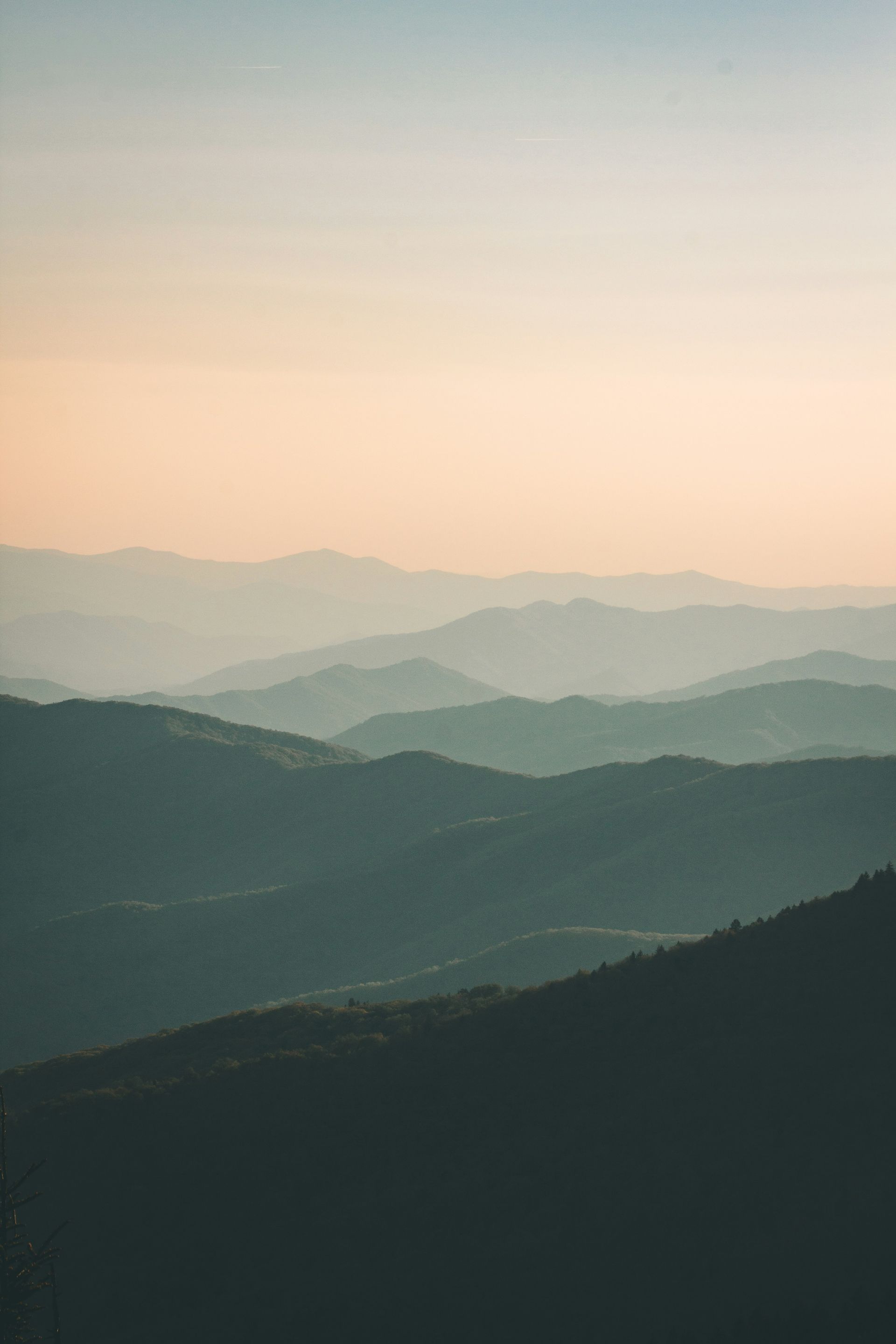 Layered mountain range fading into a pastel sky at sunset.