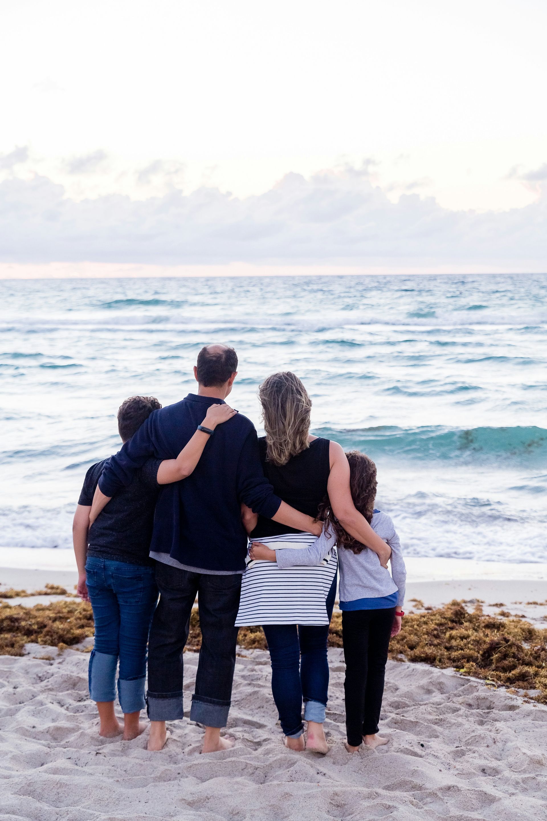 Family, arms around each other, looking at the ocean at dusk.