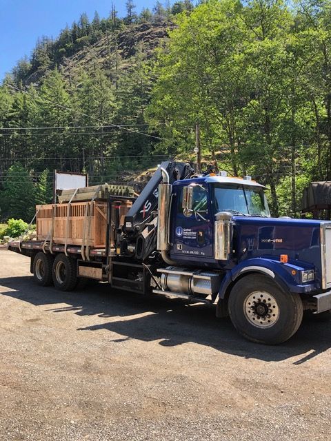 A blue truck with a crane on the back is parked in a gravel lot