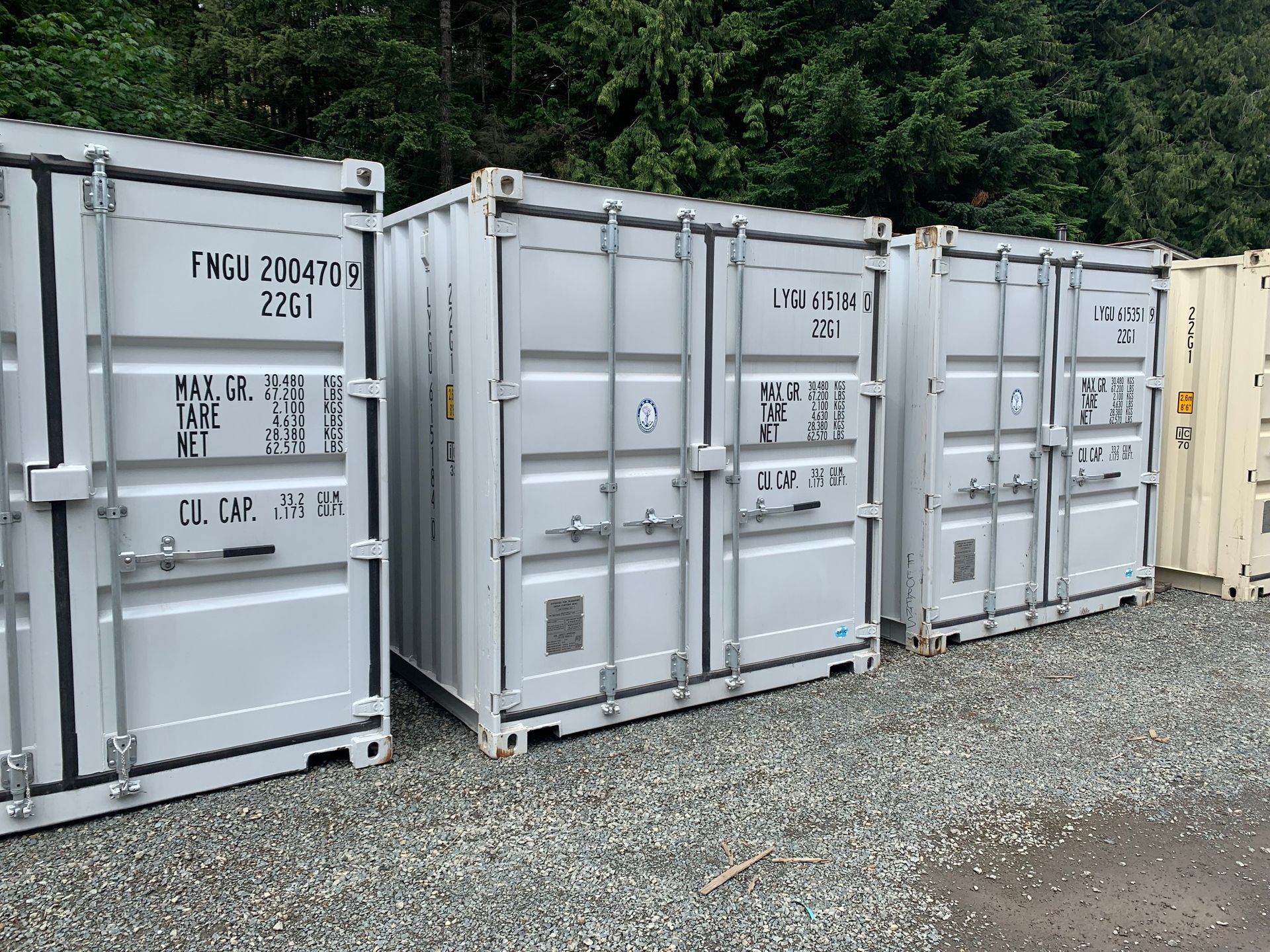 A row of shipping containers are lined up in a gravel lot.