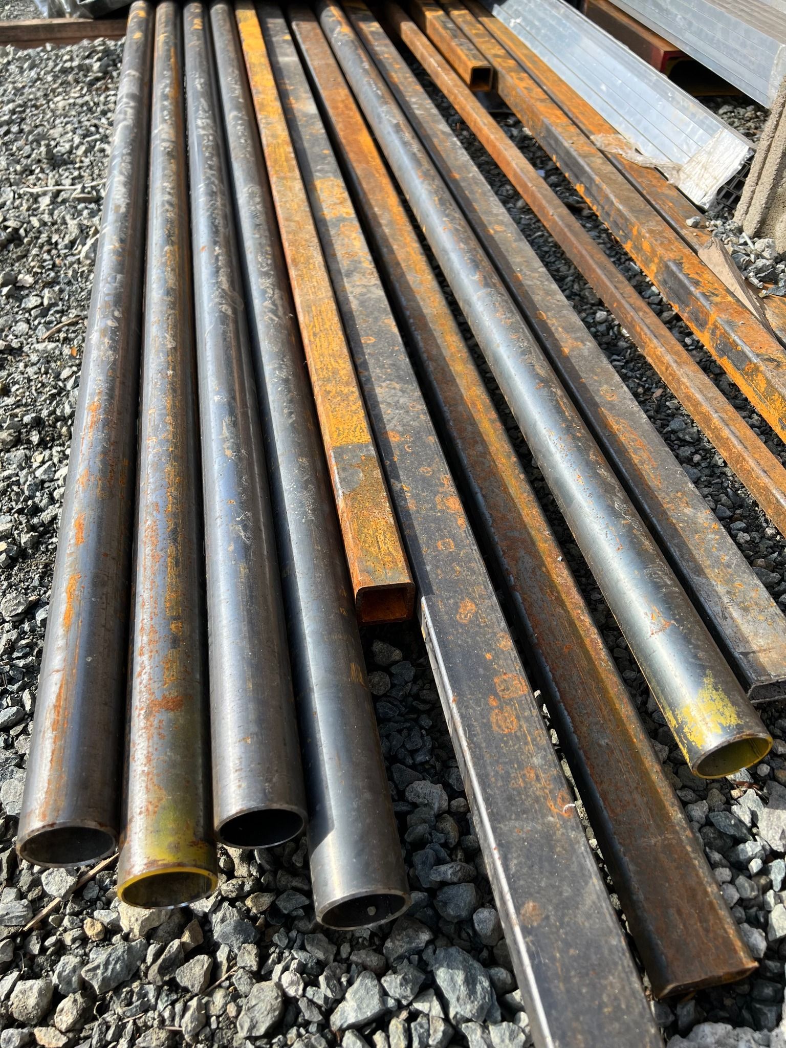 A pile of rusty metal pipes sitting on top of a pile of gravel.