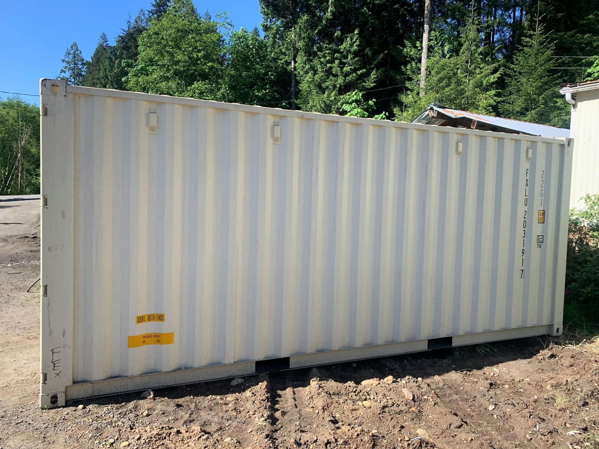 A large white shipping container is sitting in a dirt field.