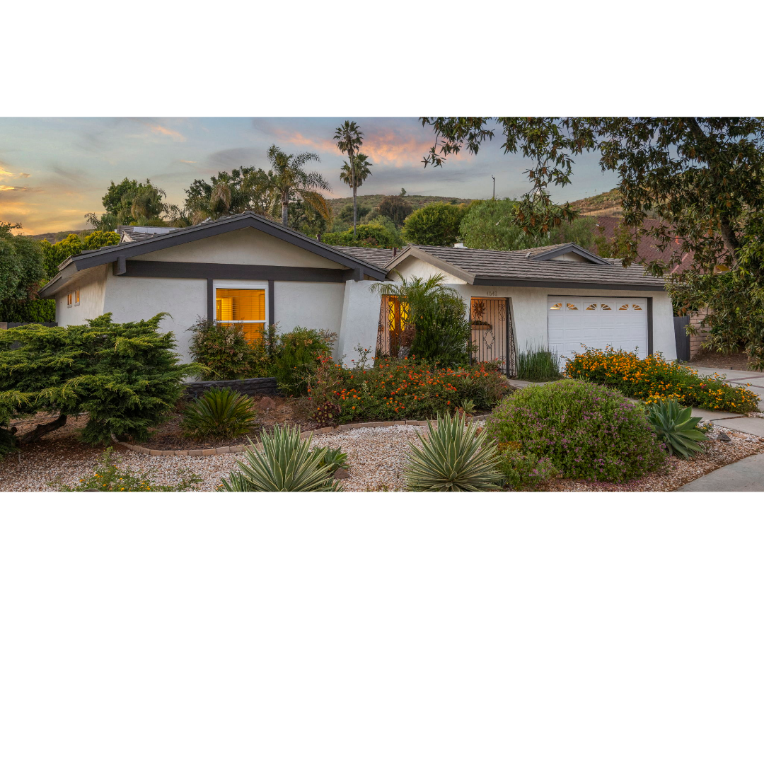 A single-story, white suburban house with a dark gabled roof, garage, and landscaped front yard at sunset.