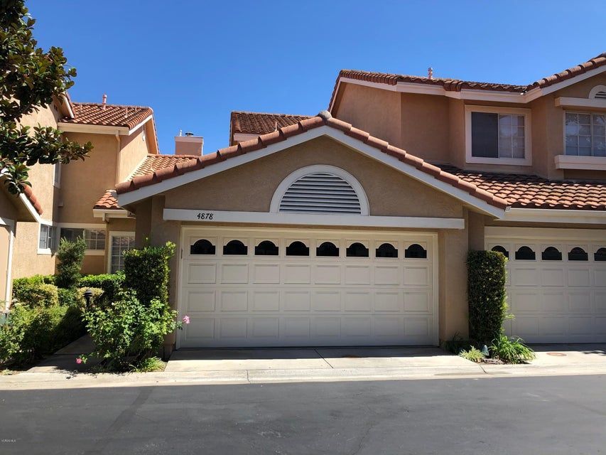 Tan-colored residential townhouses with terracotta tile roofs, prominent white garage doors, and manicured landscaping.