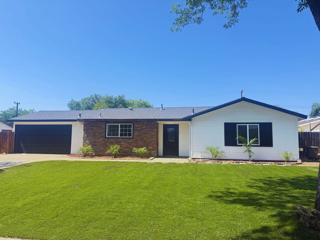 A single-story ranch-style home with a dark-roof, white siding, stone facade, and a black garage under a clear blue sky.