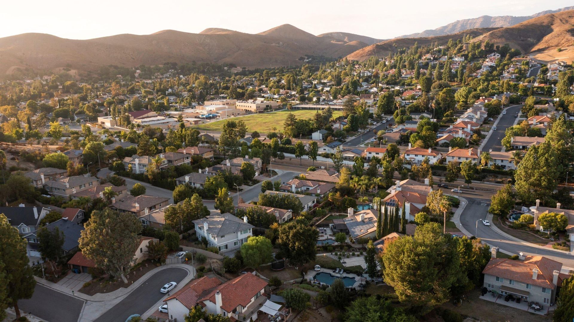 Aerial view of a hillside suburban neighborhood at sunset with winding roads and mountains in the background