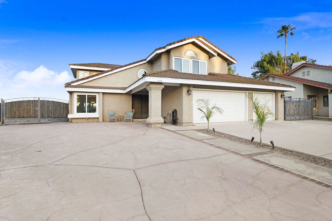 A tan, two-story house with a wide concrete driveway, white trim, a covered entryway, and a large multi-car garage.