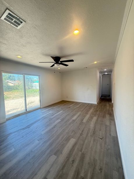 Empty living room with light wood-look flooring, white walls, sliding glass door to a yard. Ceiling fan and recessed lights.