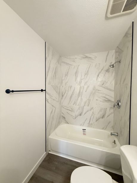 Bathroom with white tub, marble-look shower surround, and dark gray flooring.