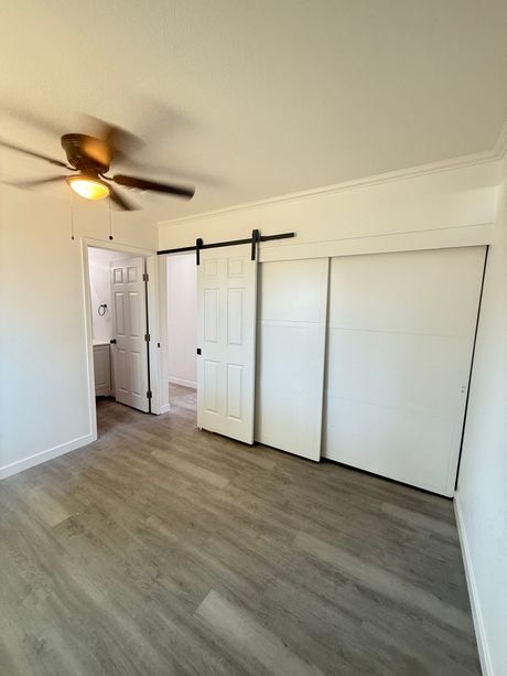 Bedroom with wood-look floor, white walls, sliding barn doors, and a ceiling fan.