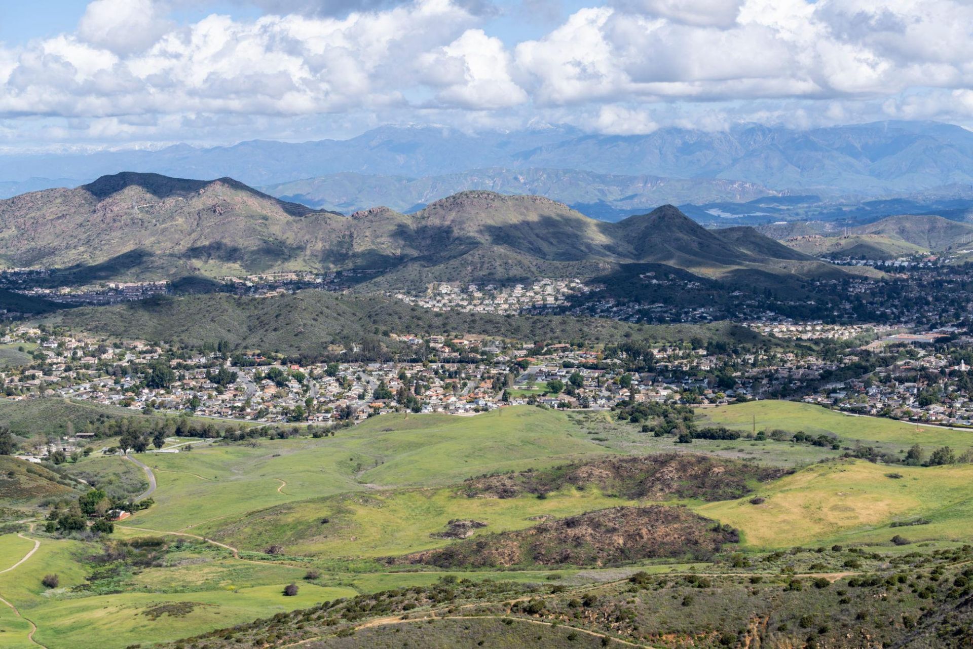 Panoramic view of a green valley town with mountains and clouds under a blue sky