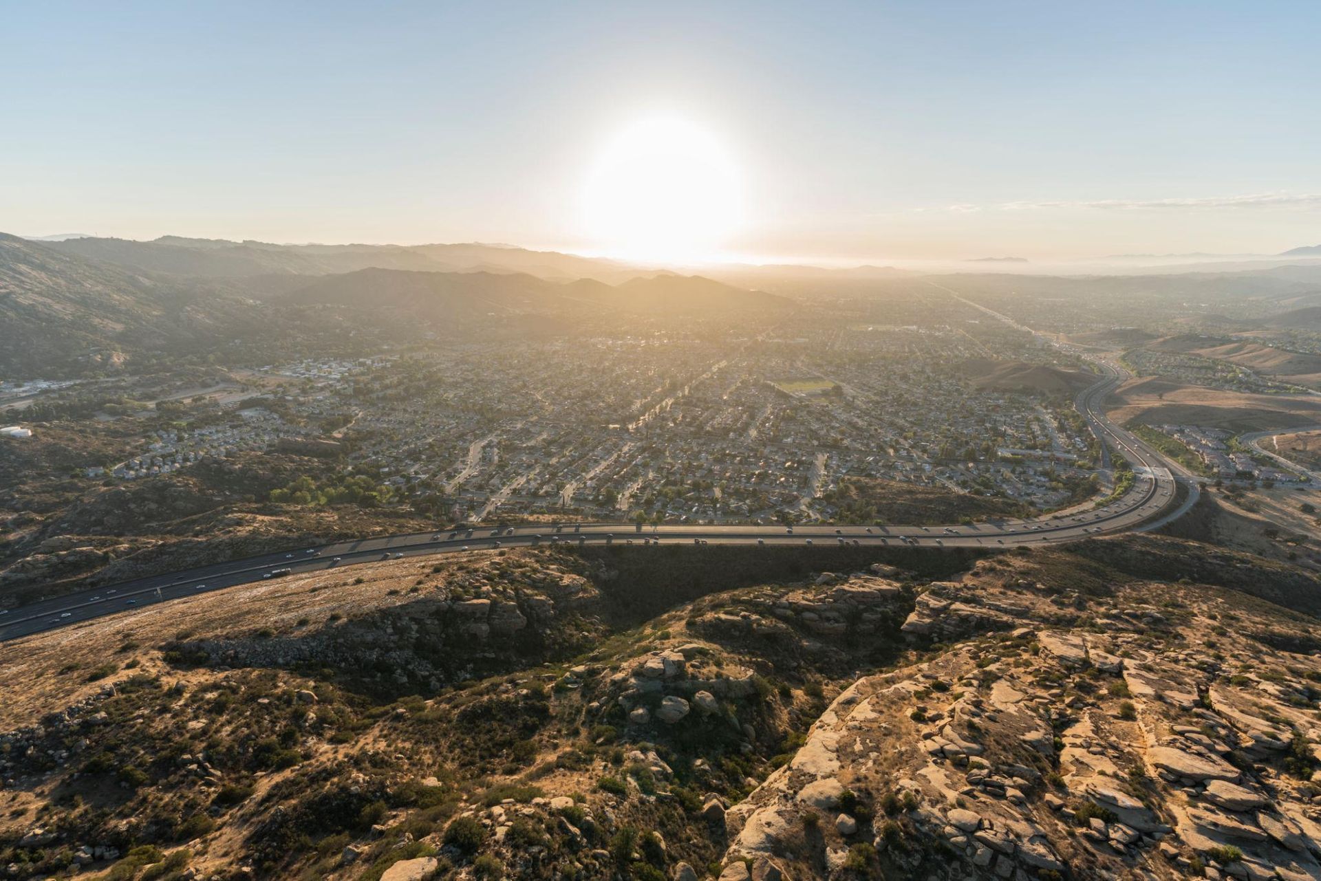 Sunrise over a sprawling city and desert hills, with roads and buildings stretching into the distance